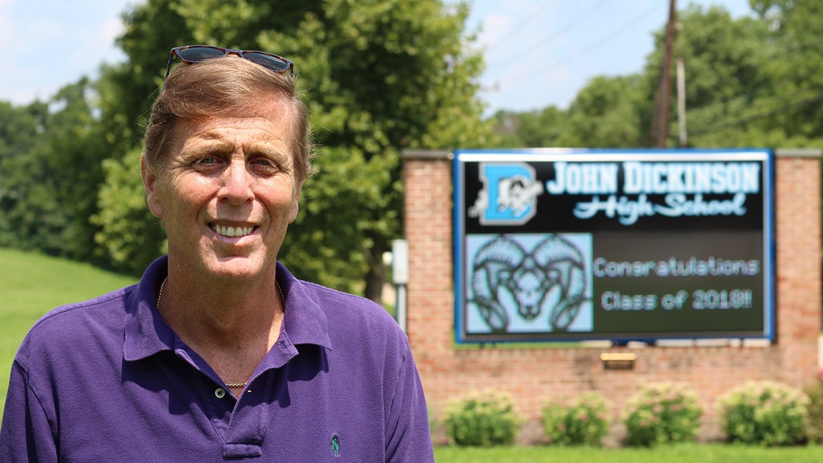 Mike Ramone smiles in front of a school building