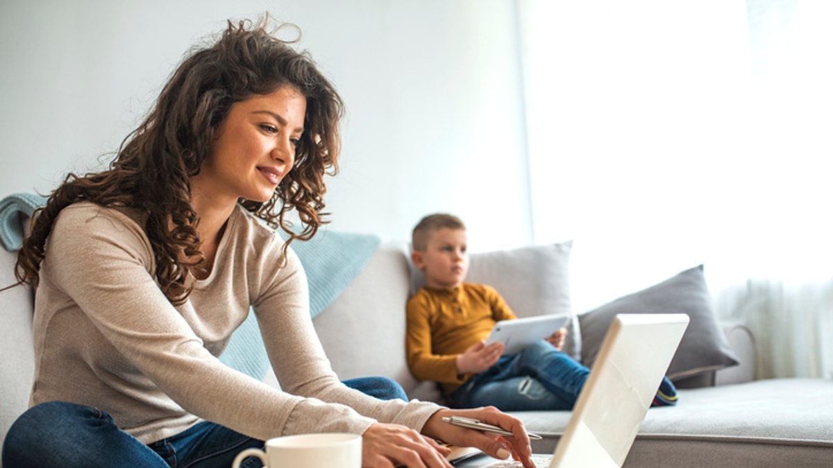 Mother works from home while her child sits on the couch