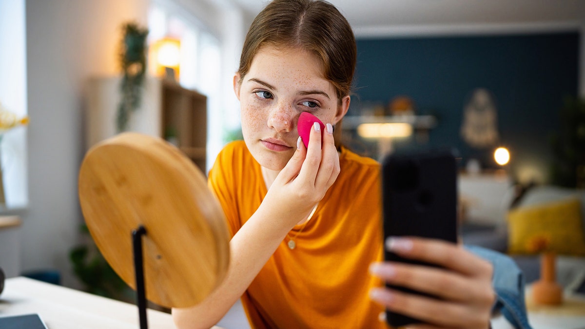 Teenage girl texting on her phone while doing make-up