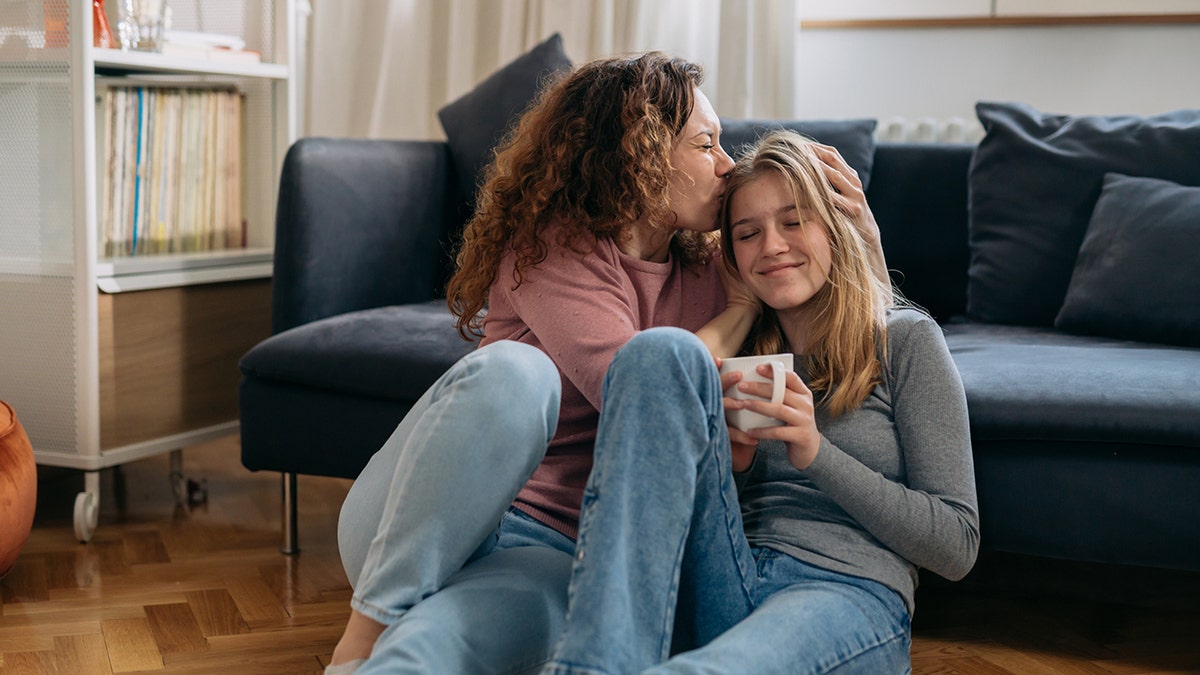 mother kiss her daughter while sitting on floor in living room