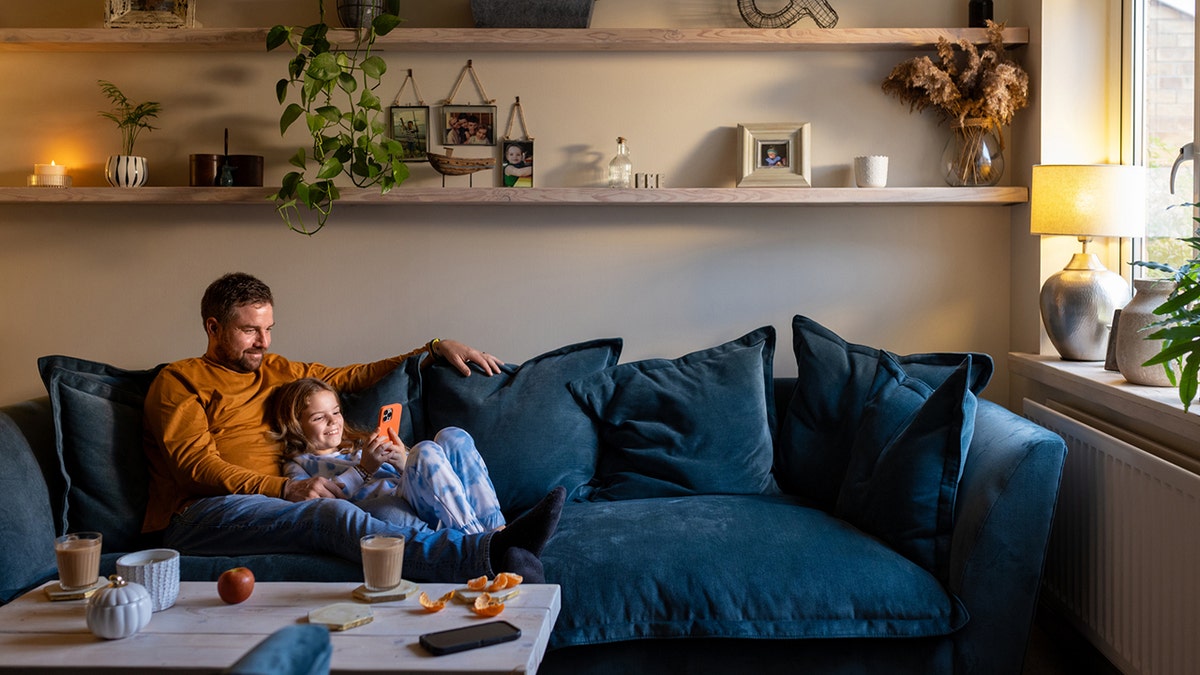 A full shot of a father lying down on the sofa with his daughter