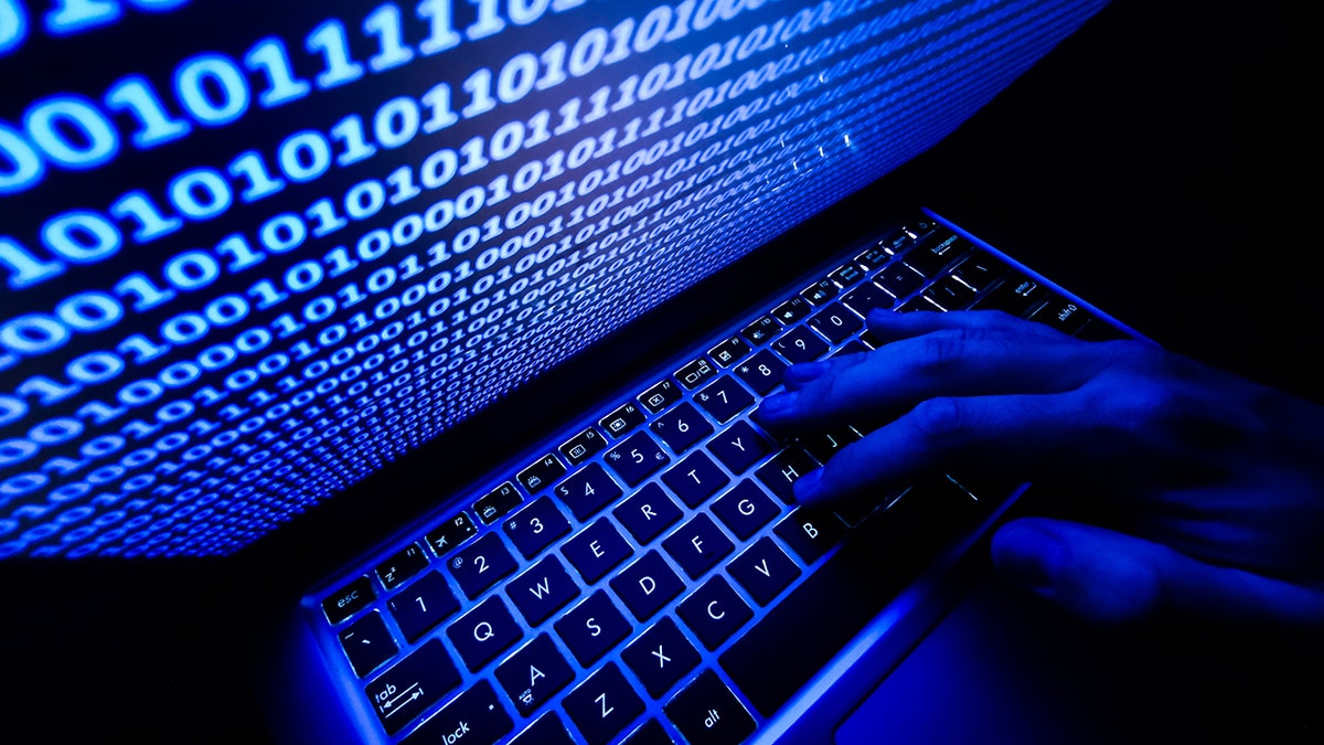 Hand typing on keyboard, with binary code displayed on computer screen