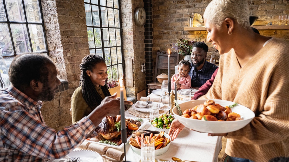 Elegant dining table with lit candles, roast turkey, potatoes, vegetables, and smiling family members.